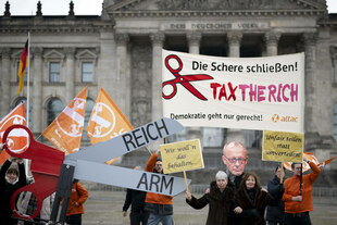 Aktivisten von attac mit Schere Reich Arm und Maske Friedrich Merz sowie Transparent Tax The Rich
