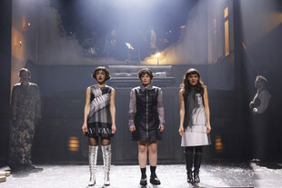 Drei Frauen in grauen Kleidern auf einer Bühne