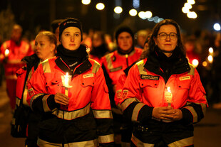Angehörige der Rettungsdienste in Arbeitskleidung halten Kerzen in den Händen