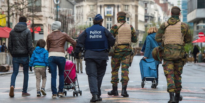 Ein Polizist und Soldaten patroullieren neben einer Gruppe von Fußgängern