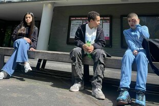 Drei Schüler:innen sitzen vor der Urania Berlin Denksporthalle