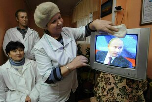 Historisches Fotos zeigt mehrere Personen an einem Fernseher, in dem Putin zu sehen ist