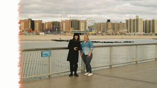 Zwei junge Frauen stehen auf einer Brücke, im Hintergrund Hochhäuser und ein Vergnügungspark