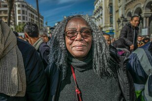 Saadia Mosbah mit grauen langen Haaren und Brille lächelt bei einer Demonstration in die Kamera
