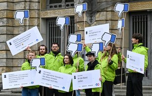 Demonstranten der Deutschen Umwelthilfe (DUH) stehen mit Plakaten und nach unten gerichteten Facebook-Daumen vor einer Klage gegen den US-Internetriesen Meta vor dem Kammergericht.