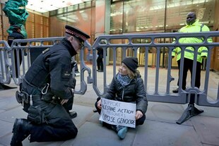 Greta Thunberg sitzt auf dem Boden und hält ein Schild, neben ihr kniet ein Polizist.