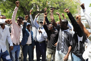 Mehrere Männer stehen nebeneinander im Freien und recken ihre Fäuste in die Luft, ein Mann hält ein Mikrofon in der Hand
