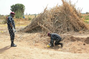 Zwei Uniformierte an einem Krater vor einem Heuhaufen.