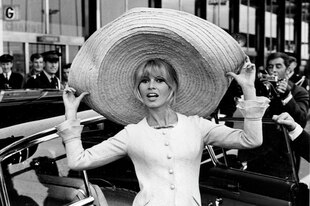 Schwarz-Weiß-Foto der jungen Brigitte Bardot mit riesigem Sombrero. Im Hintergrund eine Limousine und der Flughafen Paris-Orly