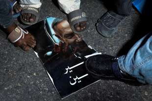 Mehrere Personen stehen auf einem zerissenen Poster, das das Gesicht von Benjamin Netanjahu zeigt