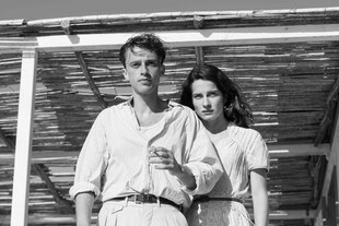 Benjamin Voisin und Rebecca Marder stehen in weißer Kleidung am Rand einer Strandpergola mit Bambusdach. Benjamin Voisin und Rebecca Marder stehen in weißer Kleidung am Rand einer Strandpergola mit Bambusdach.