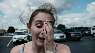 Eine Frau steht auf einem Parkplatz, sie sieht traurig aus und fasst sich an den Kopf