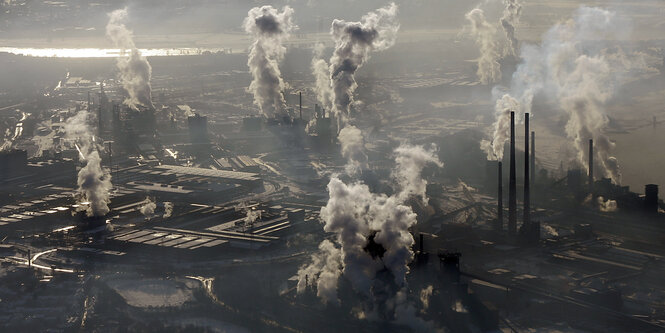 Im Vordergrund sieht man jede Menge rauchende Industrieschornsteine, die sehr viel Umweltverschmutzung produzieren. Vereinzelt sieht man kahle Bäume in der Landschaft stehen.