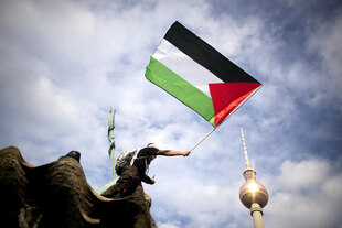 Eine Person schwingt eine Palästina Flagge, im Hintergrund sieht man den Fernsehturm