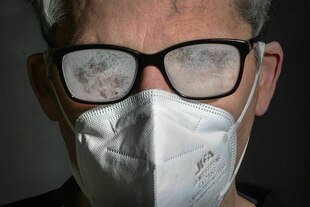 Gesicht eines mittelalten Mannes. Er trägt eine weiße FFP2-Maske. Seine Brille ist stark beschlagen
