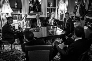 Mehrere Menschen sitzen an einem Tisch im Kreis und warten