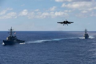 Ein Kampfjet und zwei Militärschiffe unter US-Flagge auf dem offenen Meer