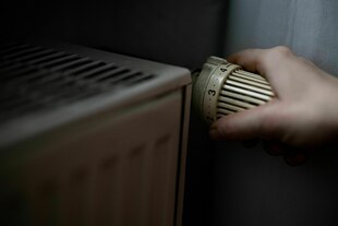 Eine Person dreht am Thermostat einer Heizung Eine Person dreht am Thermostat einer Heizung