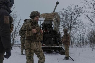 Ukrainische Soldaten stehen im Schnee neben einer Panzerhaubitze und feuern damit auf russische Stellungen