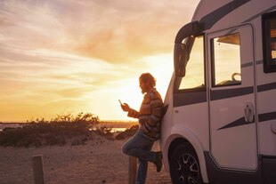 Mann lehnt in Sonnenuntergang am Strand an Campervan.