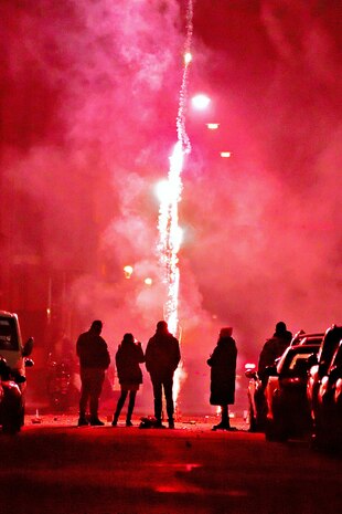 Silhouetten von Menschen auf der Straße vor einem Silvester Feuerwerk