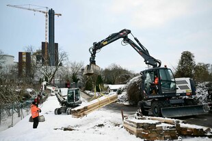 Ein Bagger nimmt während eines Stromausfalls im Südwesten Berlins vor der ausgebrannten Kabelbrücke Balken für die Baustelle auf.