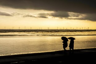 Zwei Menschen mit Regenschirmen auf einem Nordseedeich in der Abenddämmeriung