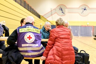 Ältere Menschen sitzen in Notunterkunft um einen Tisch