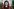 Porträtaufnahme von Lisa Vollmer. Das Foto zeigt sie mit schulterlangem, lockigen Haar und einem geraden, kürzeren Pony. Trägt ziegelroten Cardigan. Im verschwommenen Hintergrund ist eine Hauswand mit Sträuchern. Vollmers Gesicht wirkt zugewandt und freundlich.