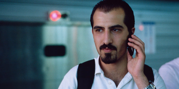 Bassel Khartabil hält sich mit der linken Hand ein Telefon ans Ohr.