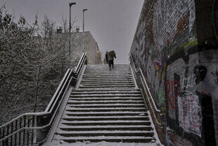 Ein Obdachloser geht bei Schneefall die Treppe zur Behmbrücke hinauf