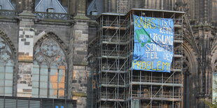 Ein Transparent hängt an einem Baugerüst am Kölner Dom.