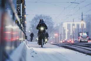 Eine Person mit Fahrrad auf einem mit Schnee bedecktem Radweg, aufgenommen waehrend starken Schneefalls in Berlin