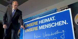 Mann in Anzug mit Brille (es ist Reiner Haseloff, Minsterpräsident von Sachsen-Anhalt, CDU) neben einem großen Schild mit der Aufschrift "Unsere Heimat. Unsere Menschen."