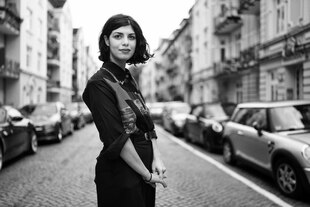 Porträt der Autorin Jegana Dschabbarowa, sie steht in einer Straßenschlucht mit Gebäuden aus der Gründerzeit und schaut freundlich.