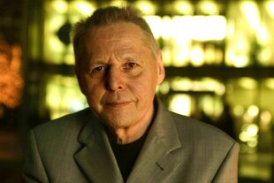 Porträt von Ulrich Enzensberger, er steht in einer Bar, hinter ihm sind unscharf Flaschen zu erkennen