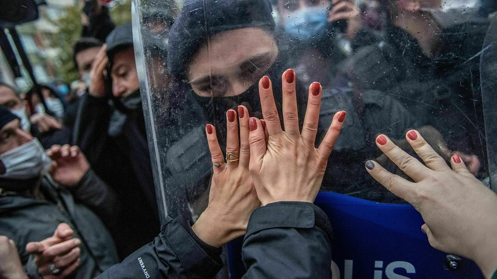 Frauenhände stemmen sich gegen das Visier eines Polizisten