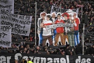 Eine Fankurve in einem Fußballstadion, die Fans halten schwarze Transparente hoch sowie eins, auf dem eine Gruppe Fans abgebildet ist mit einem Banner mit der Aufschrift: "50+1 ist unantastbar!" Eine Fankurve in einem Fußballstadion, die Fans halten schwarze Transparente hoch sowie eins, auf dem eine Gruppe Fans abgebildet ist mit einem Banner mit der Aufschrift: "50+1 ist unantastbar!"
