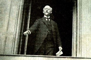 Philipp Scheidemann steht an einem offenen Fenster und spricht. Das Foto stellt vermutlich 10 Jahre später nach, wie Scheidemann am 9. November 1918 die Republik ausrief.