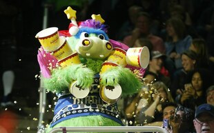 Ein bunter Drachen, das Maskottchen eines Basketballvereins, hält viele Popcorn-Becher