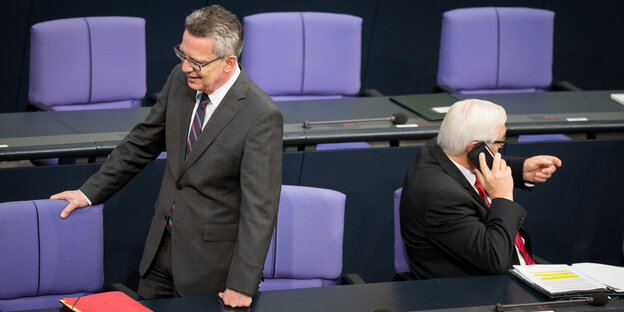 Zwei Männer im Parlament, einer sitzt, einer steht. Der Stehende ist Bundesinnenminister De Maizière, er kehrt dem Sitzenden den Rücken zu, dies ist Außenminister Frank-Walter Steinmeier (SPD)