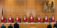 Vor einer holzgetäfelten Wand stehen acht Richter in roten Roben
