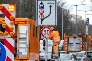 Ein Arbeiter steht in Warnkleidung auf einer Leiter und montiert ein neues ?50 km/h?-Schild an einer überfüllten Straße in München an Ein Arbeiter steht in Warnkleidung auf einer Leiter und montiert ein neues ?50 km/h?-Schild an einer überfüllten Straße in München an
