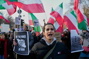 Protestaktion in Berlin, ein Heer von iranischen Flaggen, eine junge Frau, die zwei Plakate in die Kamera hält. Ein Foto fordert "Be the voice of Iran", das andere zeigt vermutlich zugedeckte Leichen von Menschen, die erschossen wurden