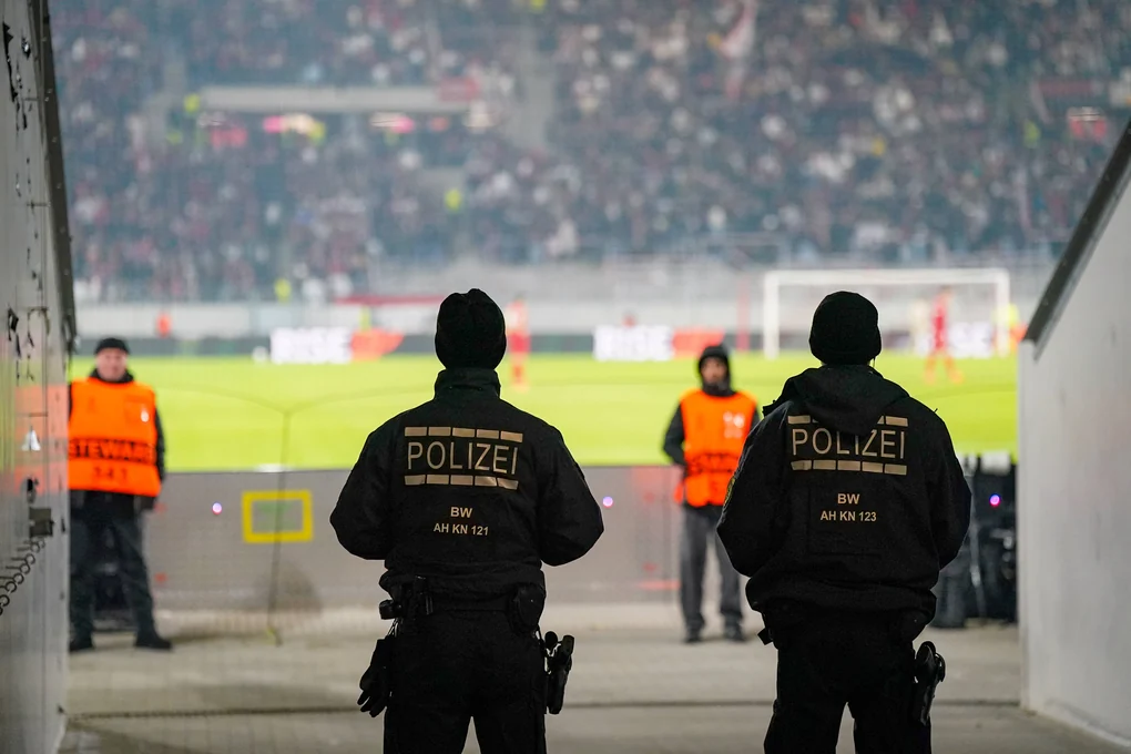 Zwei bewaffnete Polizisten, die von hinten zu sehen sind und aufs Spielfeld schauen