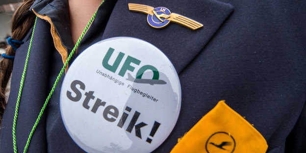 Nahaufnahme eine Buttons am Revers einer Flugbegleiterin, auf dem „UFO Streik!“ steht