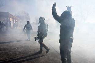 Eine Person gestikuliert gegenüber einem Uniformierten in Tränengasnebel Eine Person gestikuliert gegenüber einem Uniformierten in Tränengasnebel