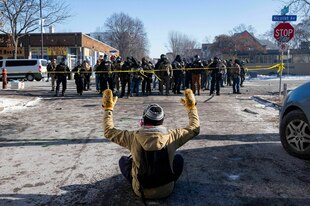 Ein Demonstrant sitzt mit erhobenen Armen auf der Straße vor Bundesbeamten in Minneapolis
