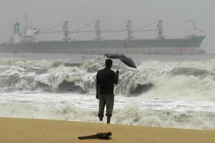 Ein Mann mit einem Regenschirm an einem Strand, er blickt auf das Meer.