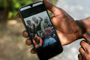 Jemand hält ein Handy, auf dem ein Foto von Geflüchteten in einem Boot zu sehen ist.